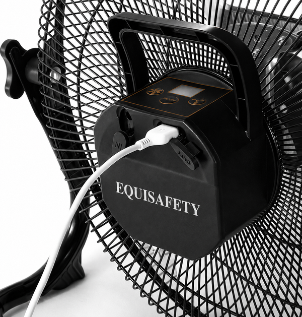 A close-up of a black EquiSafety portable fan battery pack mounted on a black wire fan, with a white power cord plugged in. The battery pack features the brand name 'EQUISAFETY' in white text on the front, a handle, and a control panel with gold accents.