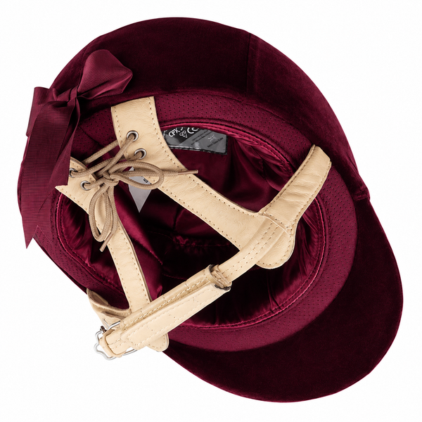 A burgundy velvet equestrian riding hat with a beige leather lacing harness and a matching satin bow, shown from a top-down view on a white background.