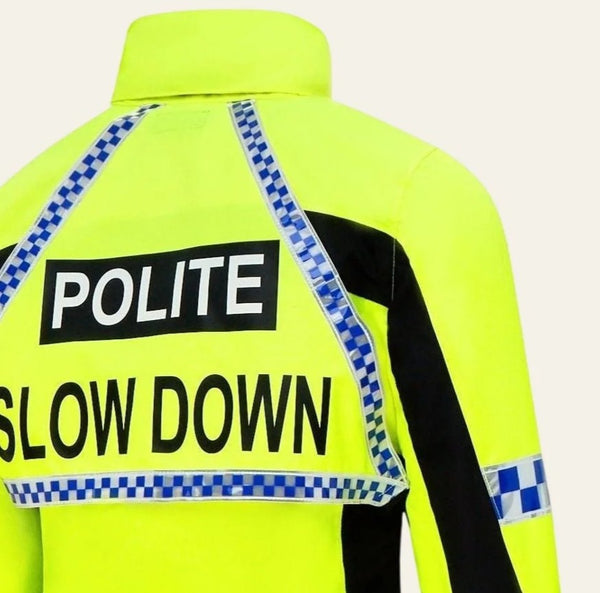 A close-up of the back of a high-visibility neon yellow jacket with blue-and-white checkered reflective strips and large black text reading 'POLITE' and 'SLOW DOWN'.